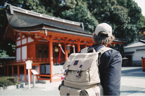 flights and travel insurance man wearing a backpack looking at a shrine in Japan